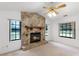 Comfortable living room with a stone fireplace, ceiling fan, and natural light through large windows at 5825 Lake Emma Ct, Groveland, FL 34736