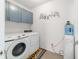 A functional laundry room with modern washer and dryer, complemented by blue cabinets and decorative wall art at 9785 Pepper Tree Trl, Wildwood, FL 34785