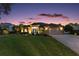 Elegant home featuring a well-manicured lawn, lovely landscaping, an attached garage, and warm exterior lighting at twilight at 13 Hickory Head Hammock, The Villages, FL 32159