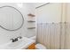 Bathroom showcasing a round mirror above the white sink, open wood shelves, and a striped shower curtain at 204 Lori Ct, Umatilla, FL 32784