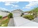 Single story home featuring a two-car garage, well manicured bushes, a driveway, and small palm tree at 2237 Jetta Way, The Villages, FL 32162