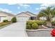 Charming single-story home with a manicured lawn, decorative shrubs, and a paved driveway leading to the garage at 2237 Jetta Way, The Villages, FL 32162