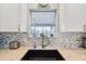 Close-up of kitchen sink with mosaic tile backsplash, granite countertop, and a window view at 2455 Five Forks Trl, The Villages, FL 32162