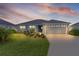 Charming single Gathering home with lush green lawn, mature plantings, and an attached two car garage at dusk at 6949 Minchew Cir, The Villages, FL 34762