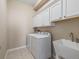 Laundry room boasts upper white cabinets, washer, dryer, and utility sink at 10927 Se 168Th Loop, Summerfield, FL 34491