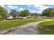 Large backyard with an outbuilding, a gravel and grass driveway, and a wooden fence with ample trees at 13033 Se 158Th Ln, Weirsdale, FL 32195