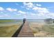 Picturesque lake view featuring a wooden dock and covered pier under a blue sky with scattered clouds at 13033 Se 158Th Ln, Weirsdale, FL 32195