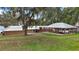 Expansive home exterior with lush lawn, mature trees, and covered parking area near the lake at 13033 Se 158Th Ln, Weirsdale, FL 32195
