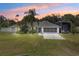 Charming single-story home with well-maintained lawn, mature landscaping, and spacious driveway at dusk at 135 N James Pl, Groveland, FL 34736
