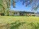 Serene backyard view highlighting the home's covered patio and lush lawn, framed by mature trees and a clear blue sky at 13700 Se 90Th Ct, Summerfield, FL 34491
