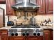 Close up of a stainless steel stove, range hood, tile backsplash, and wooden cabinets with granite countertops in the kitchen at 15733 Tower View Dr, Clermont, FL 34711