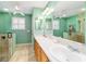 A bathroom with green walls, double sinks, a window with shutters, and a glass-door shower at 16730 Se 78Th Lillywood Ct, The Villages, FL 32162