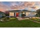 Charming single-story home featuring a red front door, well-maintained lawn, and beautiful landscaping at 16730 Se 78Th Lillywood Ct, The Villages, FL 32162
