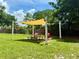 Community picnic area with a shade sail, picnic table, and red Adirondack chairs on a grassy lawn at 3607 Umbrella Tree Ln, Oxford, FL 34484