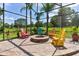 Relaxing screened-in patio area with colorful Adirondack chairs surrounding a stone fire pit at 5418 Sandy Hill Ln, Lady Lake, FL 32159