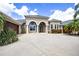Elegant stucco exterior home with arched entryway, double doors, 3-car garage, and meticulously landscaped front yard at 7303 Spring Mountain Ln, Yalaha, FL 34797