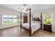 This main bedroom features a four-poster bed, wood floors, ceiling fan, and water views from large windows at 81 N Carol Ave, Mascotte, FL 34753