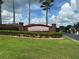Community entrance featuring brick sign, lush landscaping, and a glimpse of the gated entry and palm trees at 15509 Markham Dr, Clermont, FL 34714
