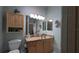 Bathroom featuring vanity with wooden cabinets, granite countertop, dual mirrors, and decorative wall cabinet at 1496 Lime Grove Ln, The Villages, FL 32162