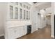 Elegant butler's pantry featuring white cabinets, glass shelving, marble backsplash, and a built-in wine fridge at 16030 Vetta Dr, Bella Collina, FL 34756