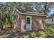 Charming brick outbuilding with a white door surrounded by lush greenery, providing extra storage or potential workshop space at 1325 Otters View Ct, Fruitland Park, FL 34731