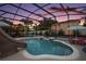 A beautiful screened pool with a slide and patio furniture sits in a private backyard under a twilight sky at 318 Stone Castle Loop, Lady Lake, FL 32159