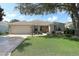 Inviting single-story home with lush green lawn, mature shade tree, and an attached two-car garage at 1412 Forest Acres Dr, The Villages, FL 32162