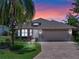Charming single Gathering home boasting a lush lawn, mature trees, and a paved driveway at dusk at 4814 Saint Andrews Arc, Leesburg, FL 34748
