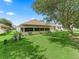 Back exterior view with screened lanai, manicured lawn, mature trees, and home features at 487 Thistledown Way, The Villages, FL 32162
