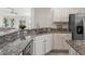 A modern kitchen is displayed with granite countertops, stainless steel appliances, and sleek white cabinets at 487 Thistledown Way, The Villages, FL 32162