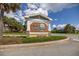 The Village of LaBelle North entrance is seen under a partly cloudy sky. Palm trees dot the landscape behind the entrance at 516 Junction Pl, The Villages, FL 32163