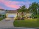 Charming home featuring a well-manicured lawn, landscaping, and a circular paver driveway at dusk at 591 Allenwood Loop, The Villages, FL 32162
