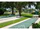 Community shuffleboard court with green and white lines is surrounded by benches, lush greenery, and a tranquil pond at 670 Fayette Ct, The Villages, FL 32162