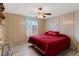 Cozy bedroom with a large window, ceiling fan and red quilted bedspread for a warm and inviting atmosphere at 717 W Coach N Four Dr, Leesburg, FL 34748