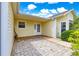 Covered back porch with brick flooring, features a white door and is surrounded by vibrant green foliage at 2450 Merida Cir, The Villages, FL 32162