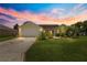 Inviting one-story home featuring a well-manicured lawn and two-car garage at sunset at 2450 Merida Cir, The Villages, FL 32162