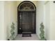 Elegant front door with decorative glass, black hardware, a 'welcome-ish' door mat, and decorative spiral shrubs at 6001 Pine Bluff Ln, Mascotte, FL 34753