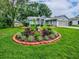 Landscaped front yard featuring a circular flower bed with vibrant plants and lush green grass at 627 Timbercrest Dr, Leesburg, FL 34748