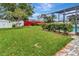 Spacious backyard with lush green lawn, red fence, manicured hedges, and screened-in patio at 1216 Cheshire St, Groveland, FL 34736