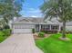 Charming single-story home featuring a well-manicured lawn, mature trees, and an attached two-car garage at 1889 Union Pl, The Villages, FL 32162