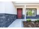 Inviting front entrance with a vibrant red door, stone accents, manicured landscaping, and modern house numbers at 13050 Ne 7Th Loop, Silver Springs, FL 34488