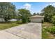 Driveway with a spacious two-car garage, set amidst a green yard and mature trees under a bright sky at 9879 Sw 38Th Ave, Ocala, FL 34476