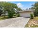 Two-car garage with a wide driveway, nestled in a grassy yard with mature trees and a clear blue sky at 9879 Sw 38Th Ave, Ocala, FL 34476