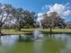 Beautiful pond with a fountain, surrounded by mature trees and a clear blue sky, creating a serene landscape at 2680 Clubhouse Dr, Lake Wales, FL 33898