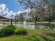 Scenic view of a lush pond with a fountain surrounded by mature trees and green grass at 2680 Clubhouse Dr, Lake Wales, FL 33898