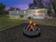 Backyard with a built-in fire pit, wooden fence, and porch with white railing at dusk at 2391 Buck Board Trl, Lake Wales, FL 33898