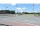 Outdoor tennis courts with nets and lighting, surrounded by fencing and green landscaping under a bright sky at 1077 Medinah Way, Winter Haven, FL 33884