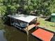 Boat dock with covered lift, seating, and a red floating dock surrounded by clear water and lush greenery at 1422 Avenue H Sw, Winter Haven, FL 33880