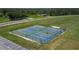 A fenced in set of tennis and pickleball courts are ready for a day of play, surrounded by lush green grass and trees at 7591 Limonia Dr, Indian Lake Estates, FL 33855