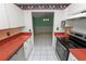 Galley kitchen with white cabinetry, red countertops, tile flooring, and stainless steel appliances at 7101 Scenic Pl, Lakeland, FL 33810